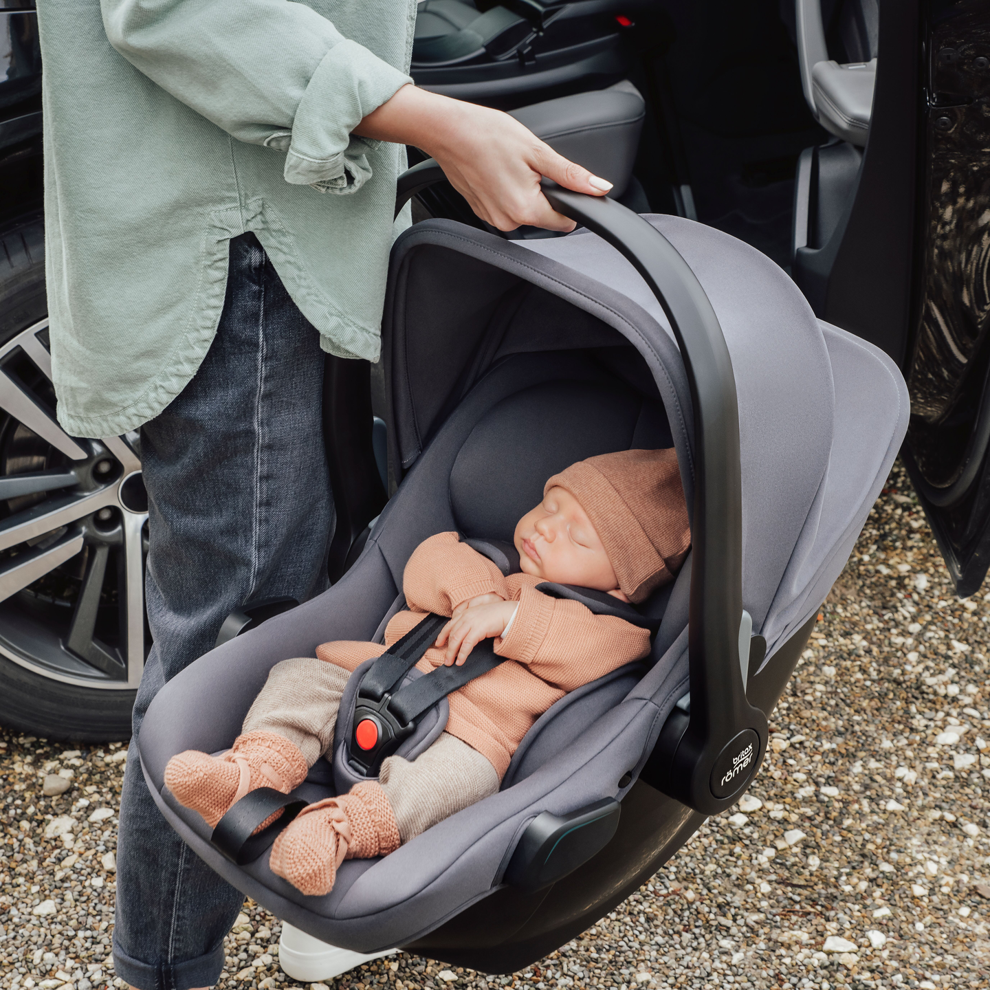 A parent carries a sleeping baby secured in a Baby-Safe Core car seat next to the car.